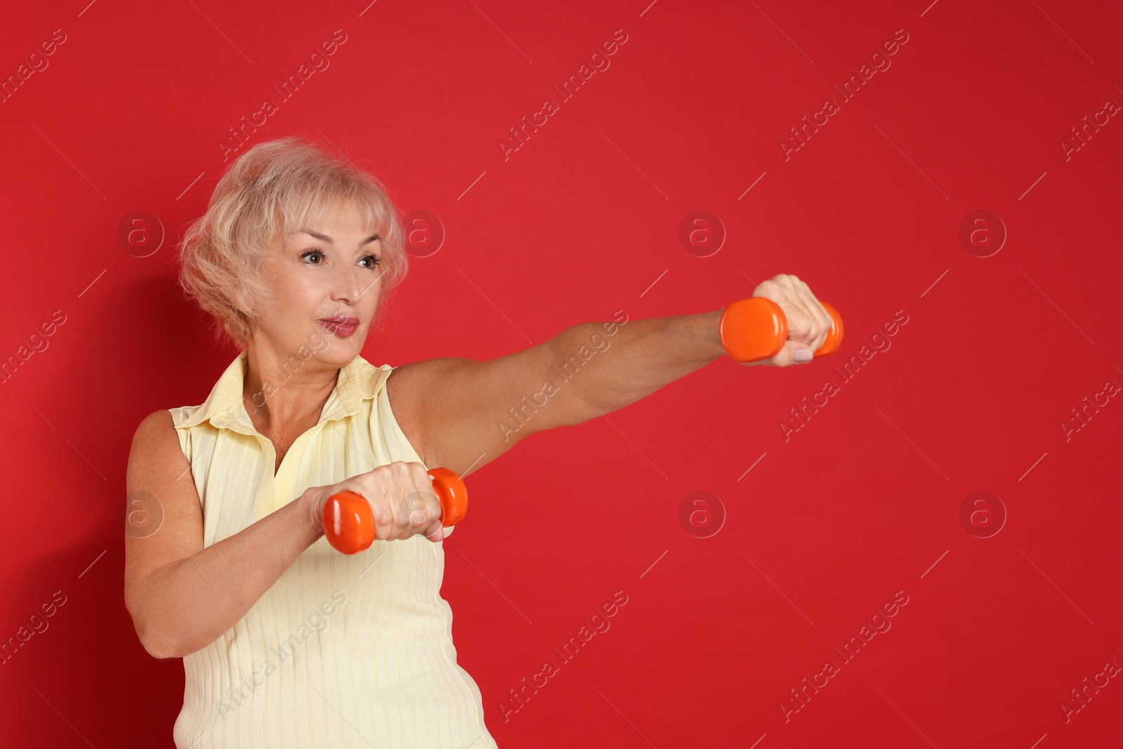 Photo of Senior woman exercising with dumbbells on red background, space for text