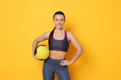 Smiling woman with fitness ball on yellow background