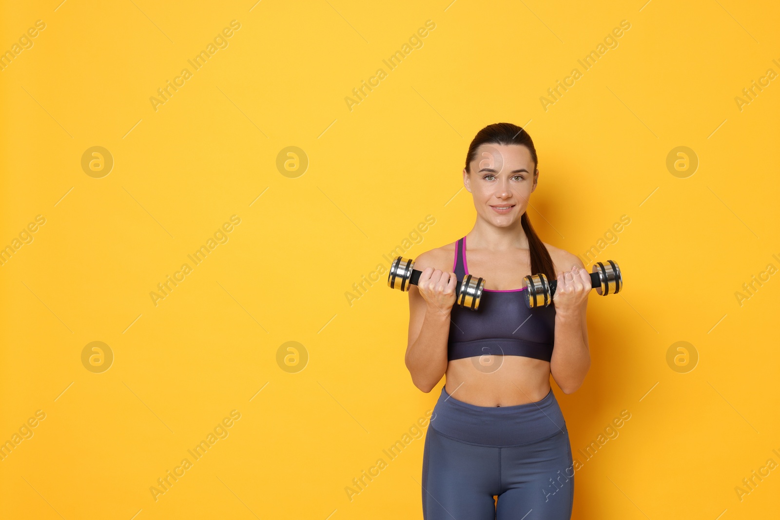 Photo of Smiling woman with dumbbells training on yellow background. Space for text