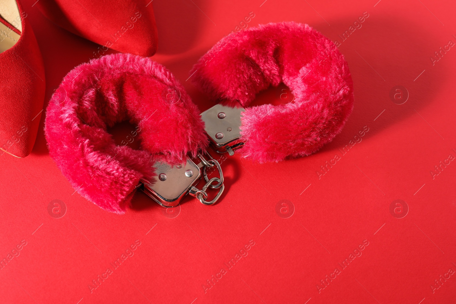 Photo of Pink fluffy handcuffs and high-heeled shoes on color background, flat lay