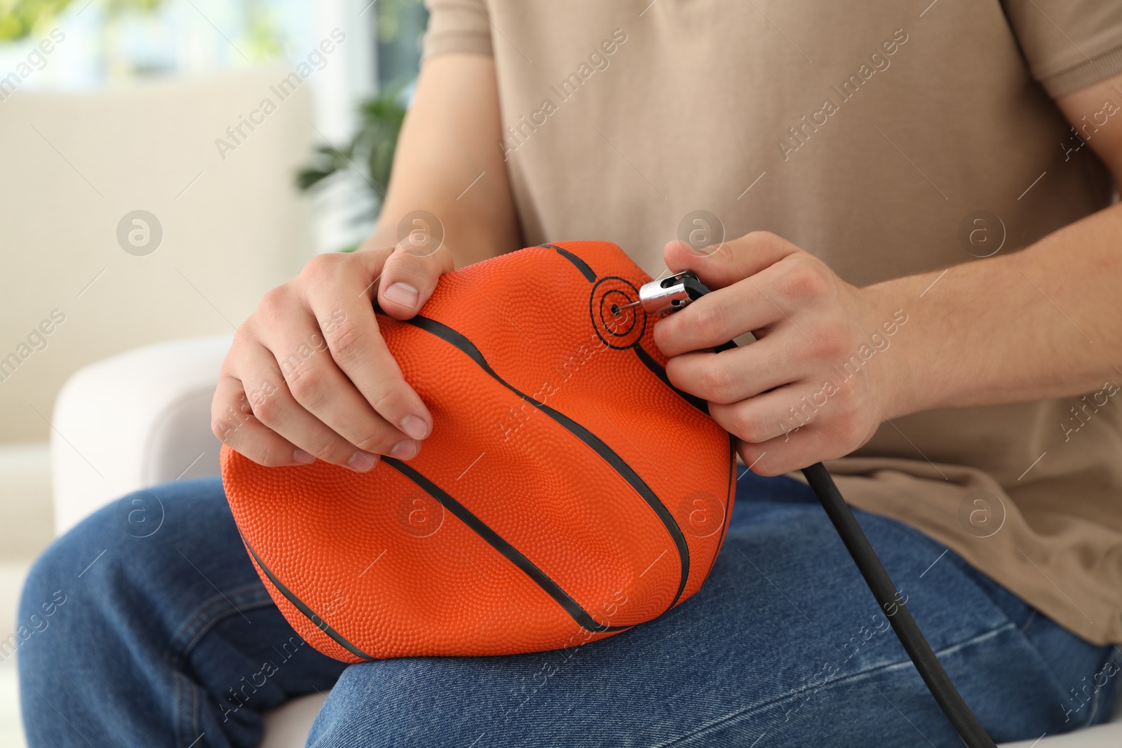 Photo of Man inflating basketball ball with air compressor indoors, closeup