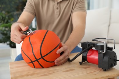 Photo of Man inflating basketball ball with air compressor indoors, closeup