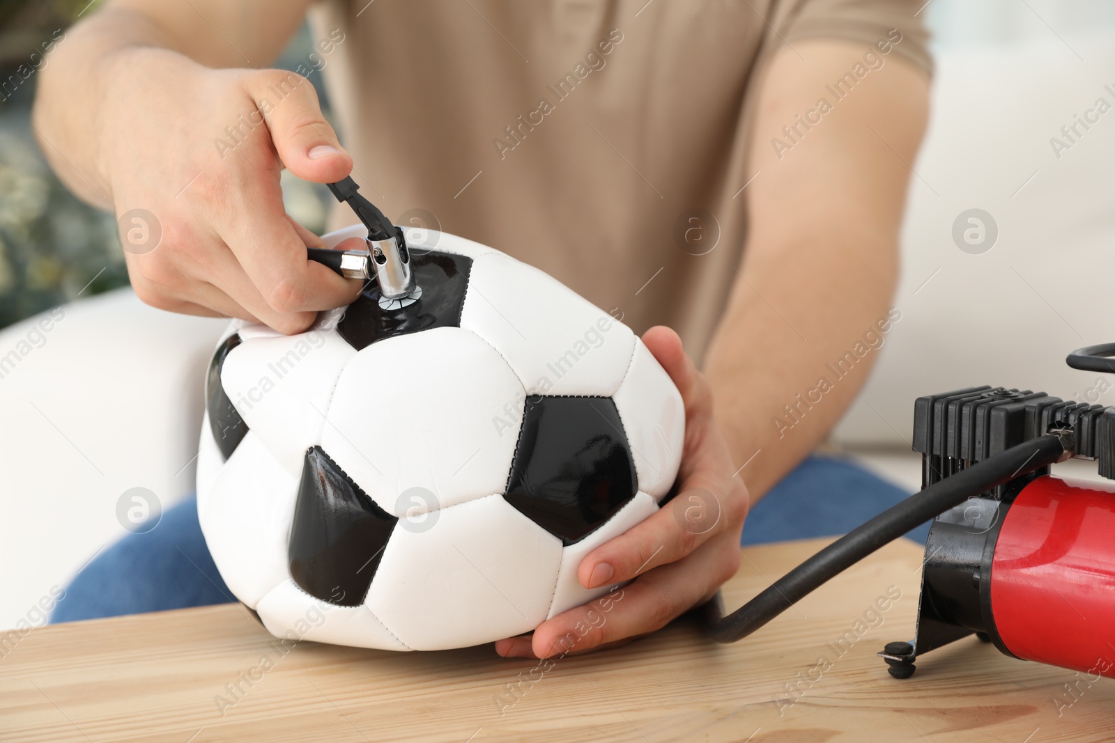 Photo of Man inflating soccer ball with air compressor indoors, closeup