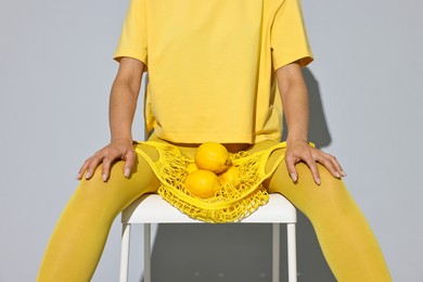 Photo of Woman with net bag and lemons on chair against light grey background, closeup