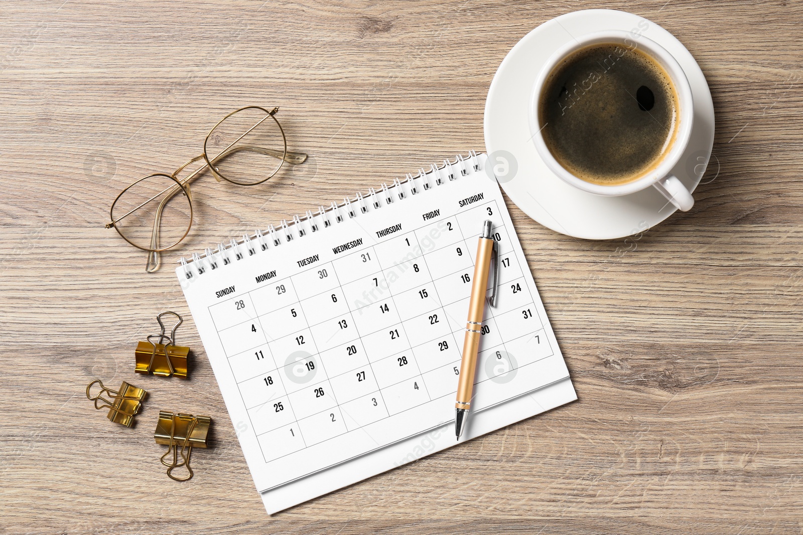 Photo of Timetable. Monthly planner, glasses, coffee, pen and clips on wooden table, flat lay