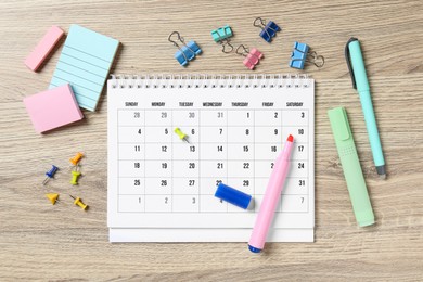 Photo of Timetable. Monthly planner and stationery on wooden table, flat lay