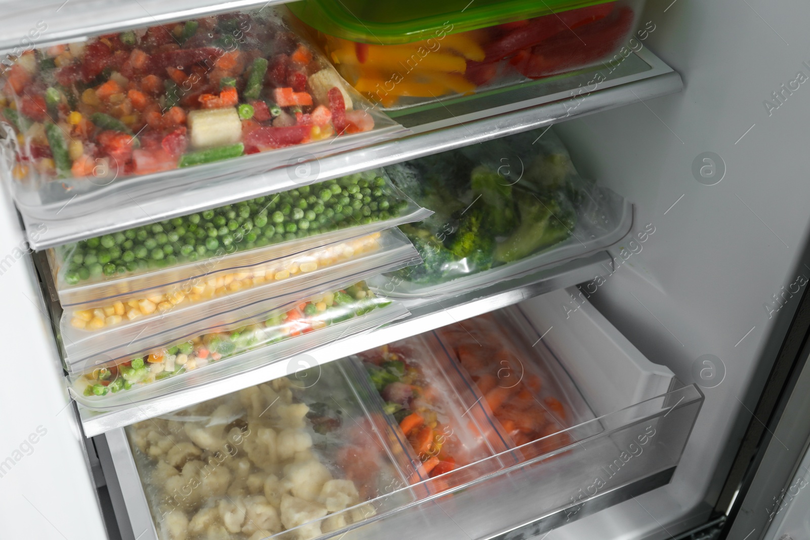 Photo of Plastic bags and glass container with different frozen vegetables in refrigerator