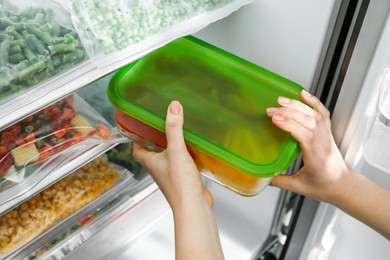 Photo of Woman taking glass container with frozen cut bell pepper from refrigerator, closeup