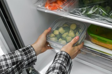 Photo of Woman taking glass container with frozen chopped zucchini from refrigerator, closeup