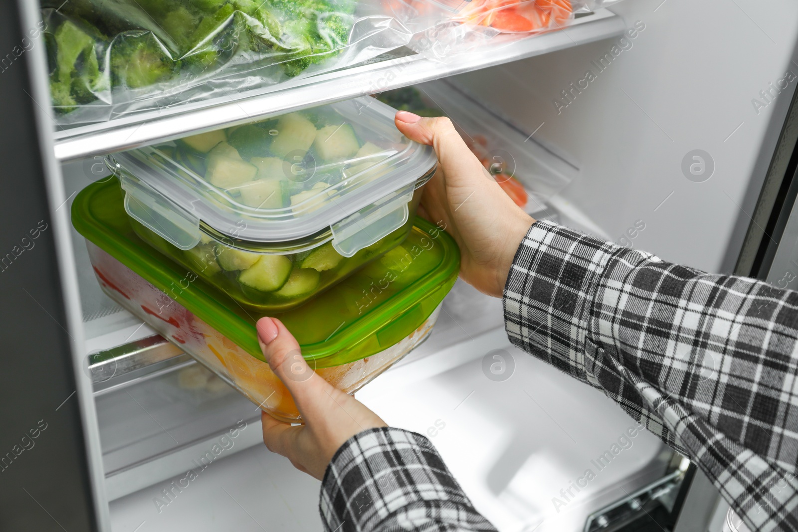 Photo of Woman taking glass containers with frozen vegetables from refrigerator, closeup