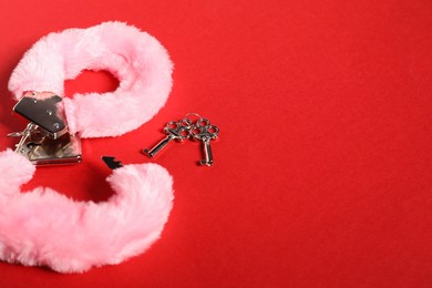 Photo of Pink fluffy handcuffs and keys on red background, space for text