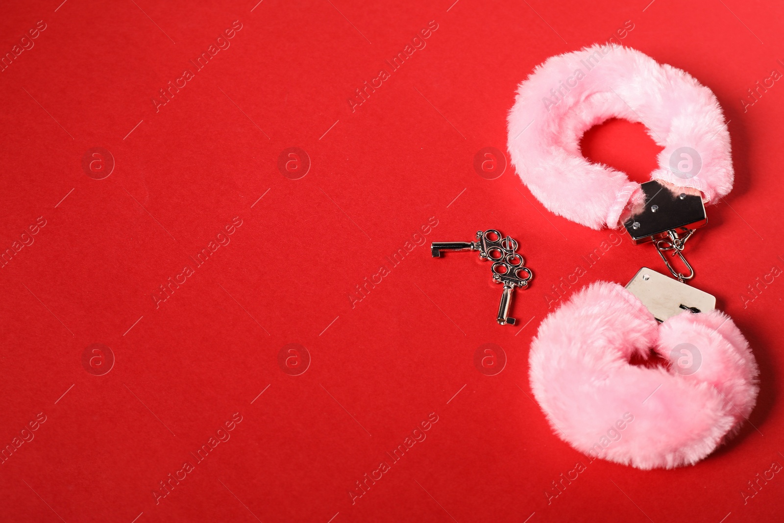 Photo of Pink fluffy handcuffs and keys on red background, space for text