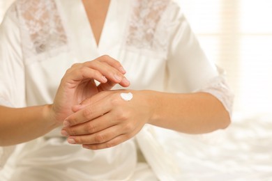 Photo of Woman applying cream onto hand at home, closeup