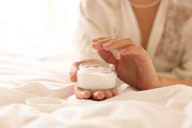 Photo of Woman with jar of cream on bed at home, closeup. Space for text