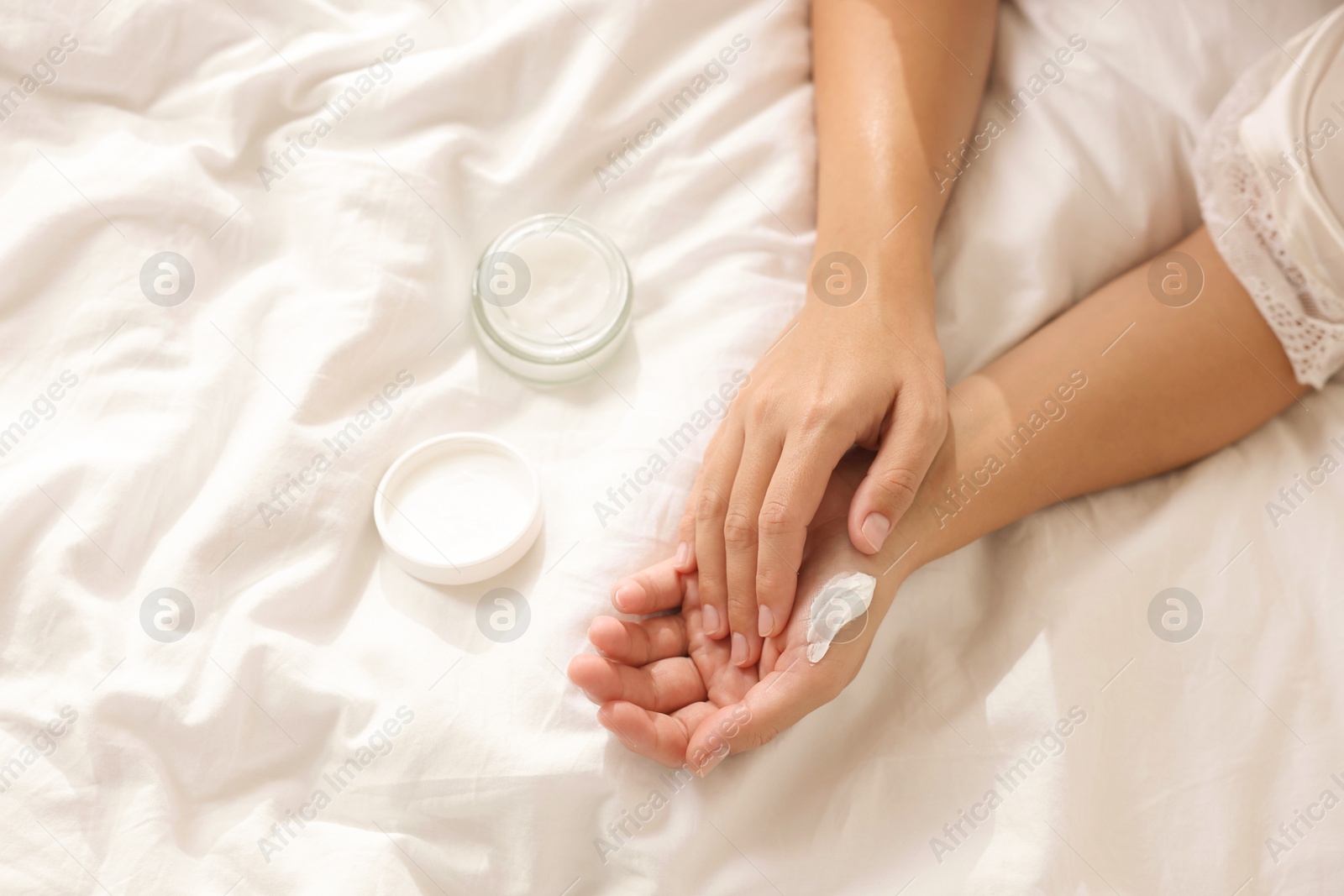 Photo of Woman applying cream onto hand on bed at home, top view