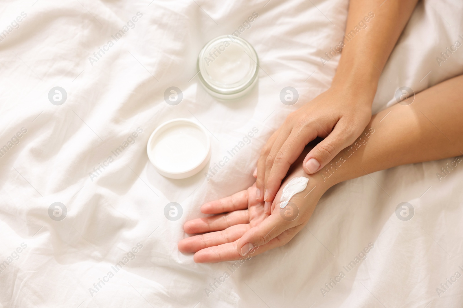 Photo of Woman applying cream onto hand on bed at home, top view