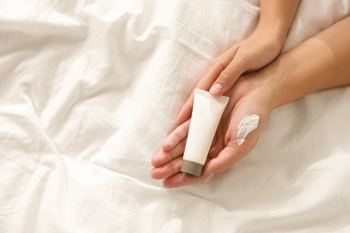 Photo of Woman with tube of cream on bed at home, top view. Space for text