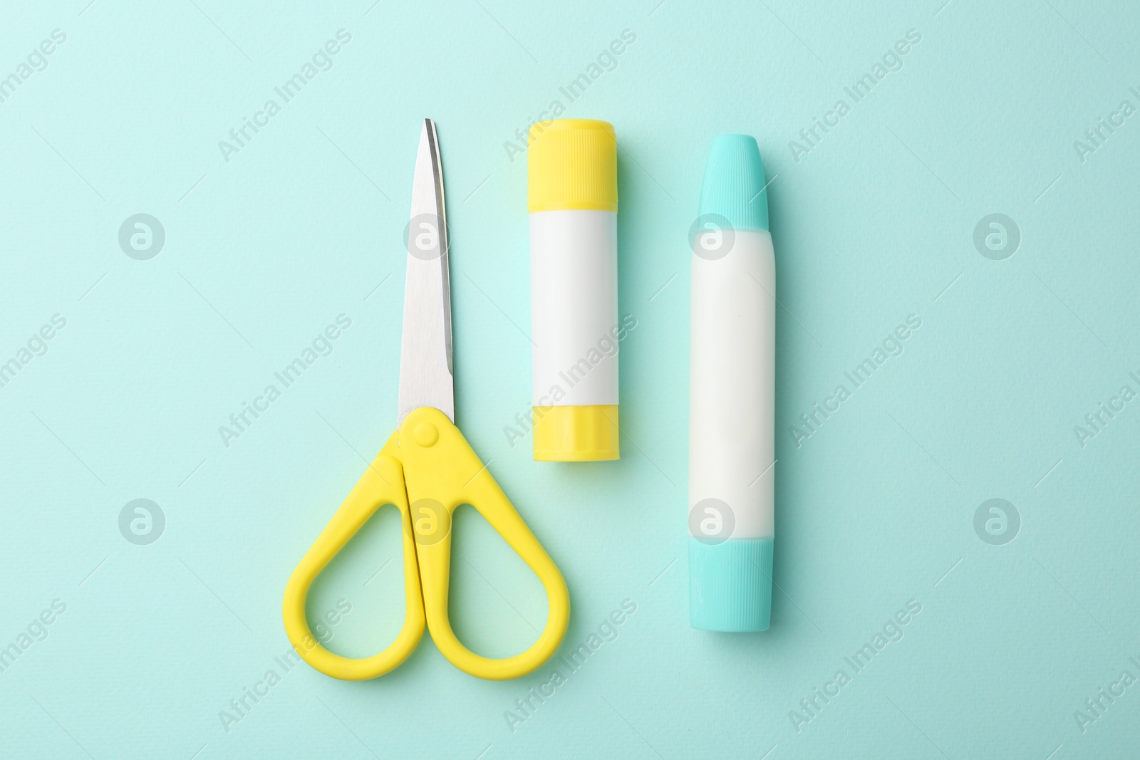 Photo of Glue and scissors on turquoise background, flat lay