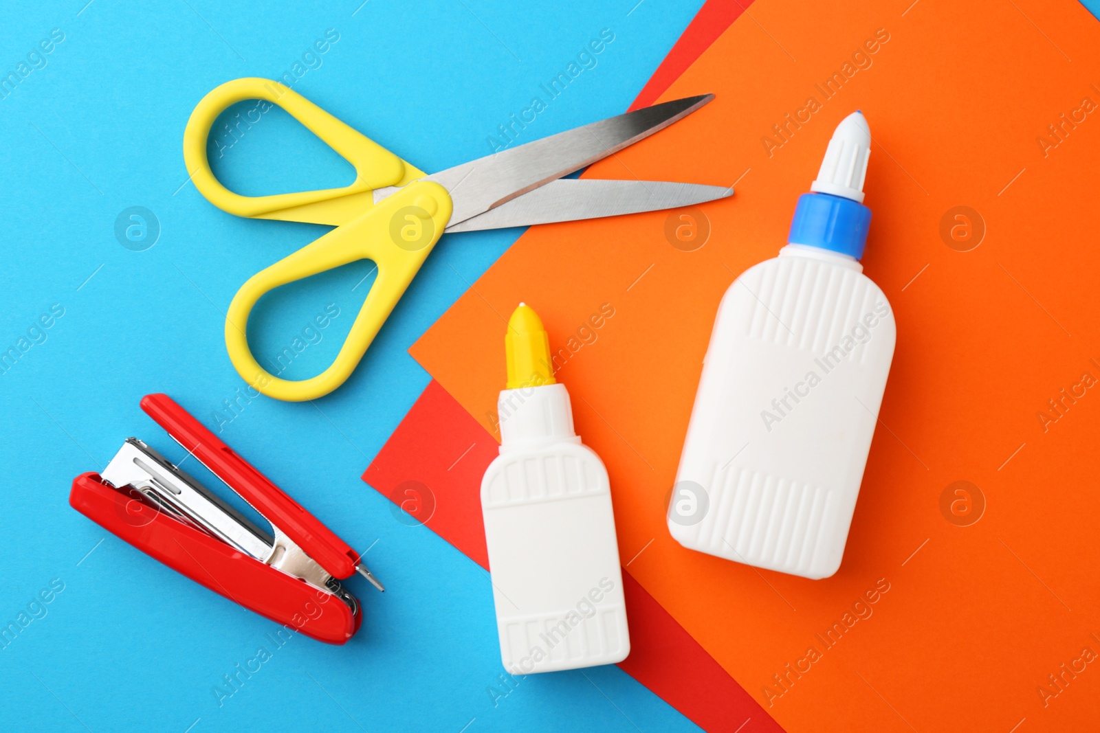 Photo of Glue, colorful paper, stapler and scissors on light blue background, flat lay