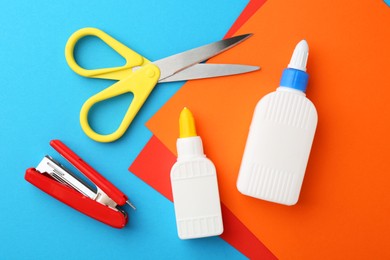 Photo of Glue, colorful paper, stapler and scissors on light blue background, flat lay