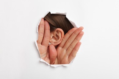 Woman showing hand to ear gesture through hole in white paper, closeup