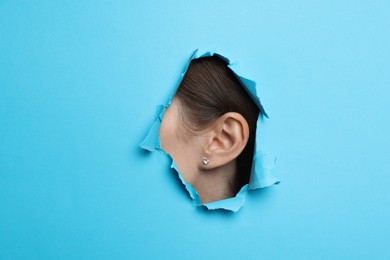 Woman showing her ear through hole in light blue paper, closeup