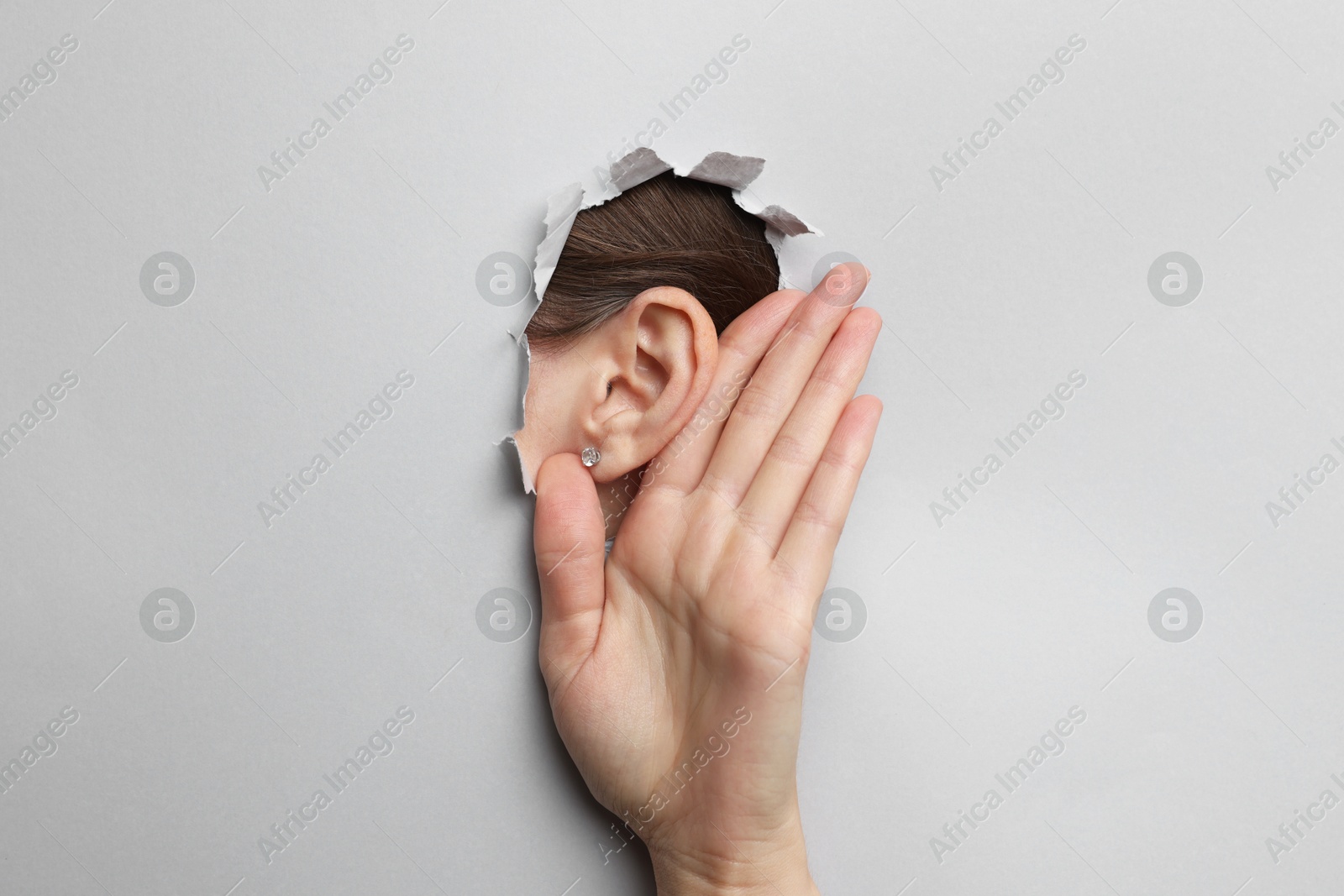 Photo of Woman showing hand to ear gesture through hole in grey paper, closeup