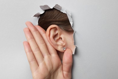 Photo of Woman showing hand to ear gesture through hole in grey paper, closeup