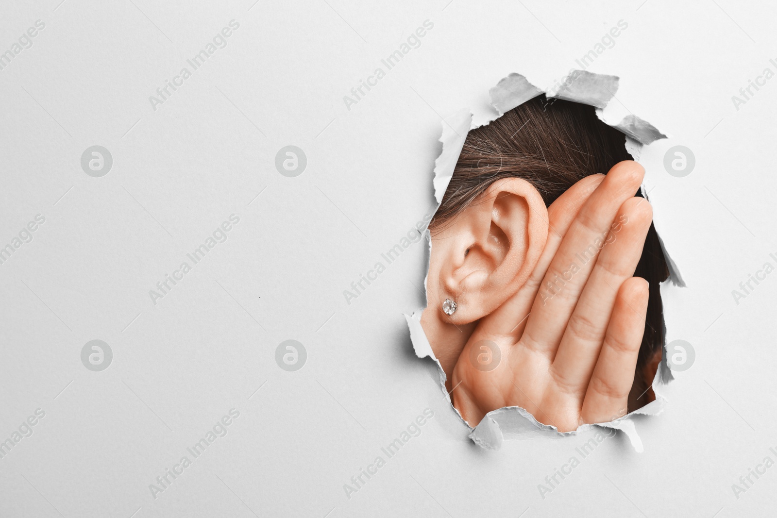 Photo of Woman showing hand to ear gesture through hole in grey paper, closeup. Space for text