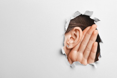 Photo of Woman showing hand to ear gesture through hole in grey paper, closeup. Space for text