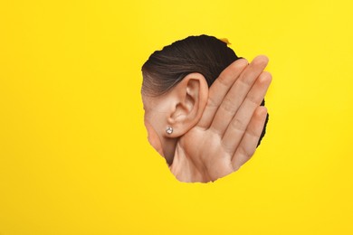 Woman showing hand to ear gesture through hole in yellow paper, closeup