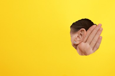 Woman showing hand to ear gesture through hole in yellow paper, closeup. Space for text