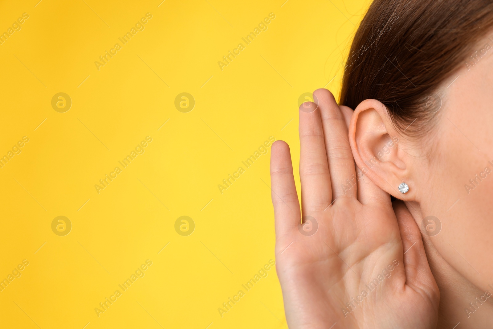 Photo of Woman showing hand to ear gesture on yellow background, closeup. Space for text