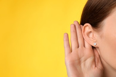 Woman showing hand to ear gesture on yellow background, closeup. Space for text