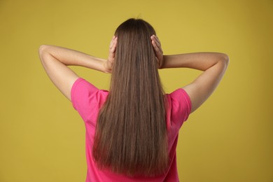 Woman covering her ears on dark yellow background, back view