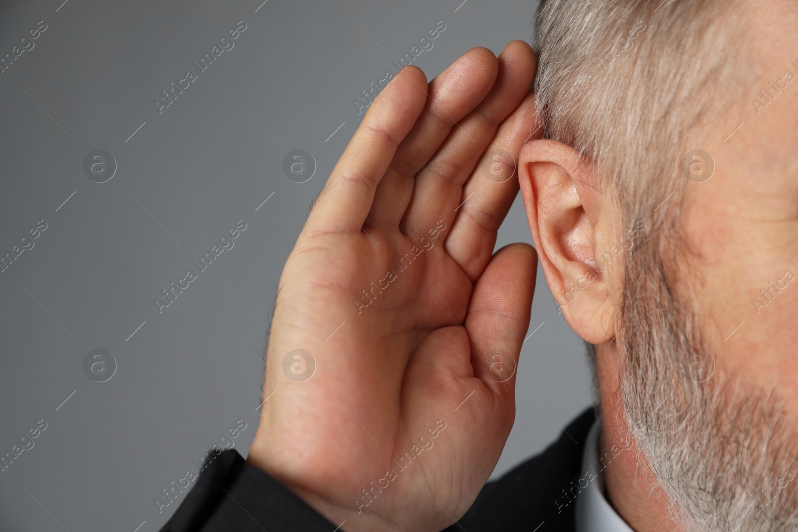 Photo of Senior man showing hand to ear gesture on grey background, closeup. Space for text