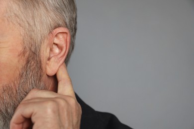 Photo of Senior man showing hand to ear gesture on grey background, closeup. Space for text