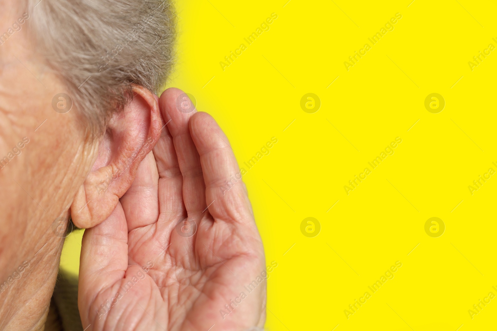 Photo of Senior woman showing hand to ear gesture on dark yellow background, closeup. Space for text