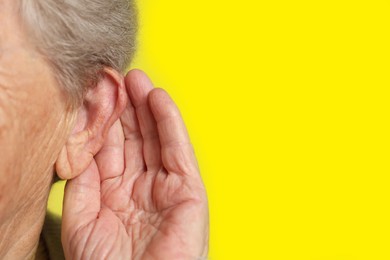 Photo of Senior woman showing hand to ear gesture on dark yellow background, closeup. Space for text