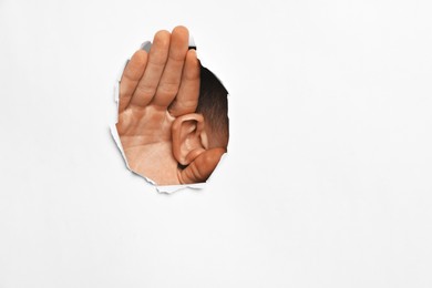 Photo of Man showing hand to ear gesture through hole in white paper, closeup. Space for text