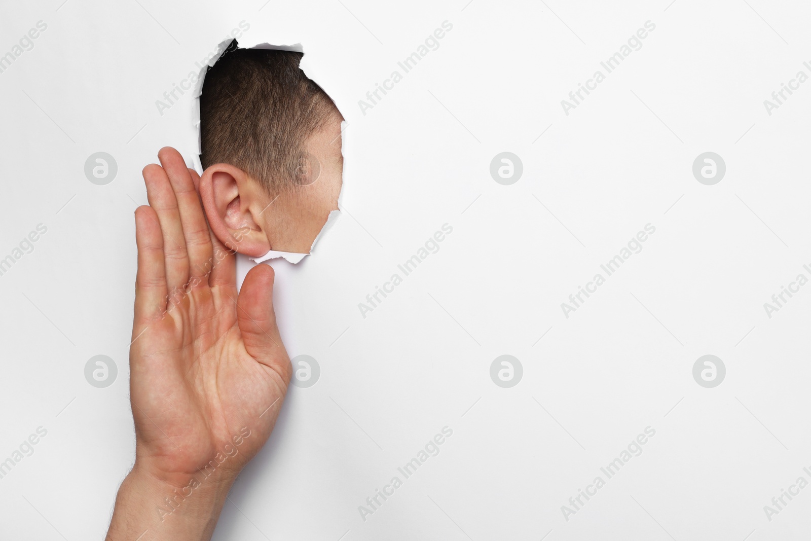 Photo of Man showing hand to ear gesture through hole in white paper, closeup. Space for text