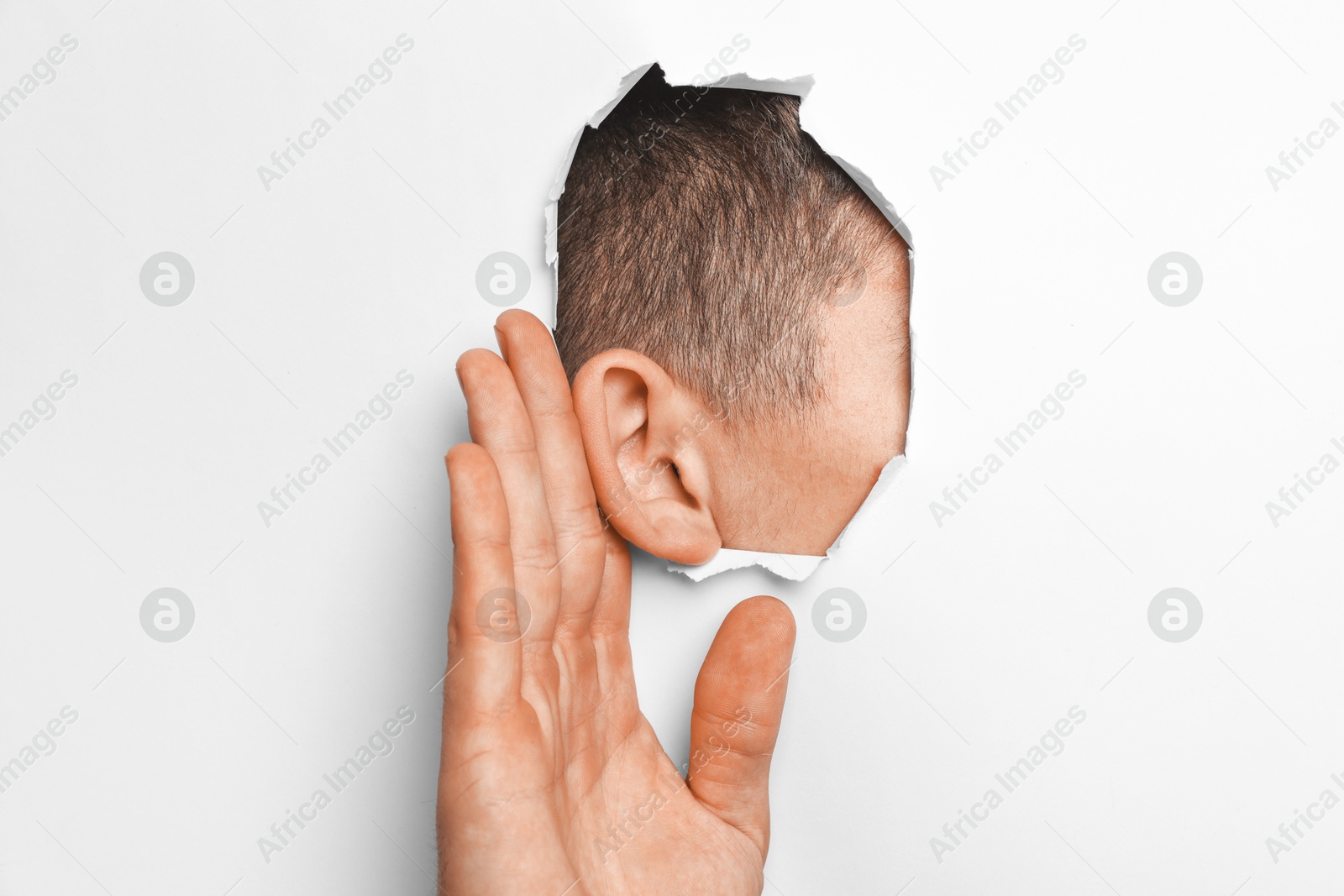 Photo of Man showing hand to ear gesture through hole in white paper, closeup