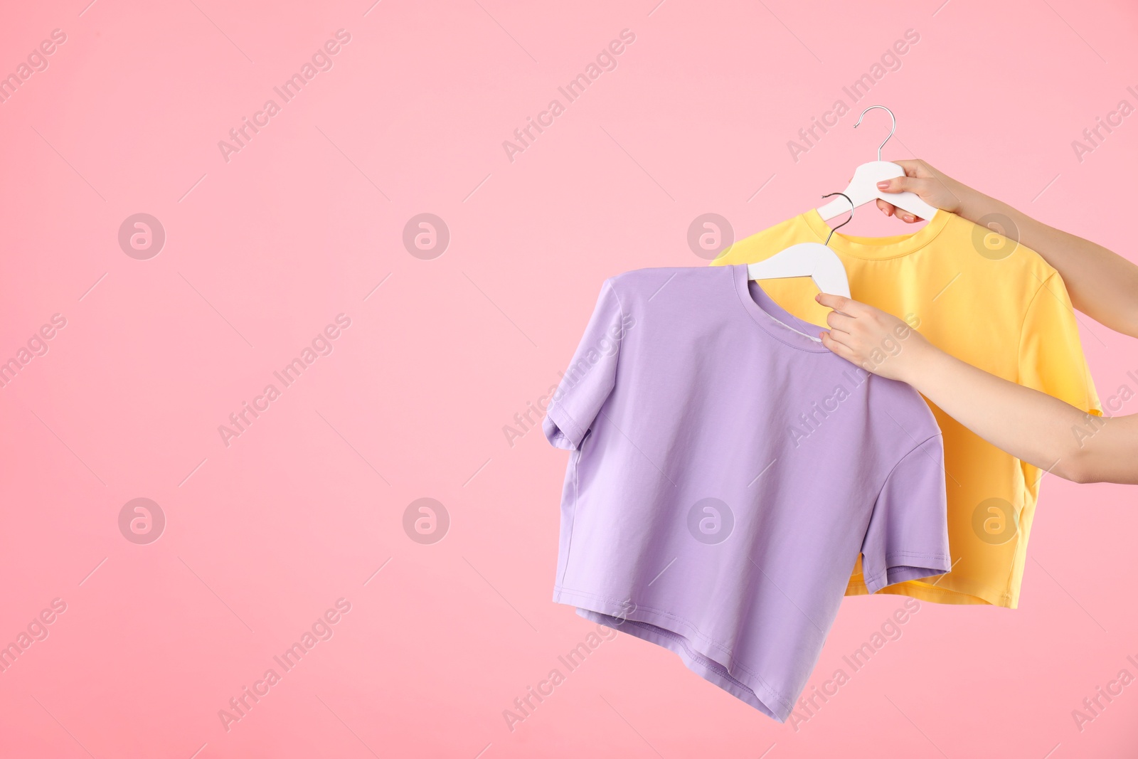 Photo of Woman holding hanger with colorful t-shirts on pink background, closeup. Space for text