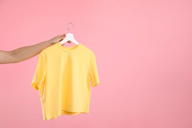 Photo of Woman holding hanger with yellow t-shirt on pink background, closeup. Space for text