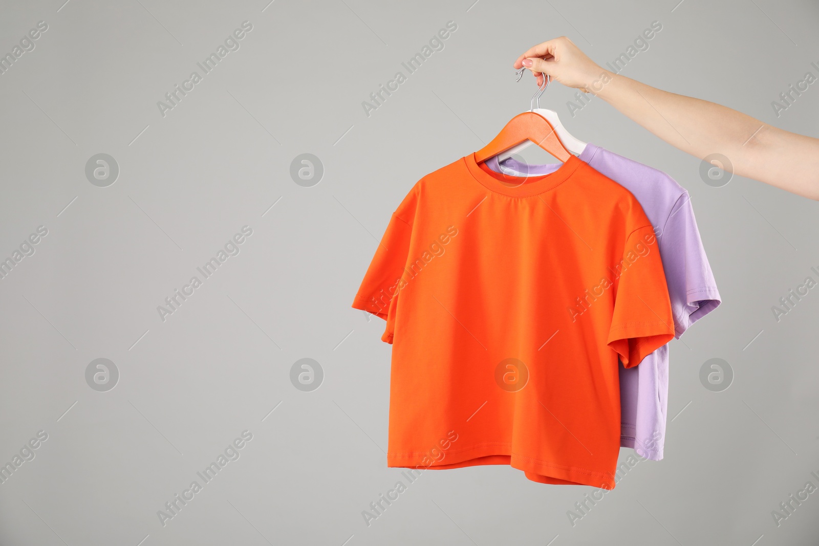 Photo of Woman holding hanger with colorful t-shirts on grey background, closeup. Space for text