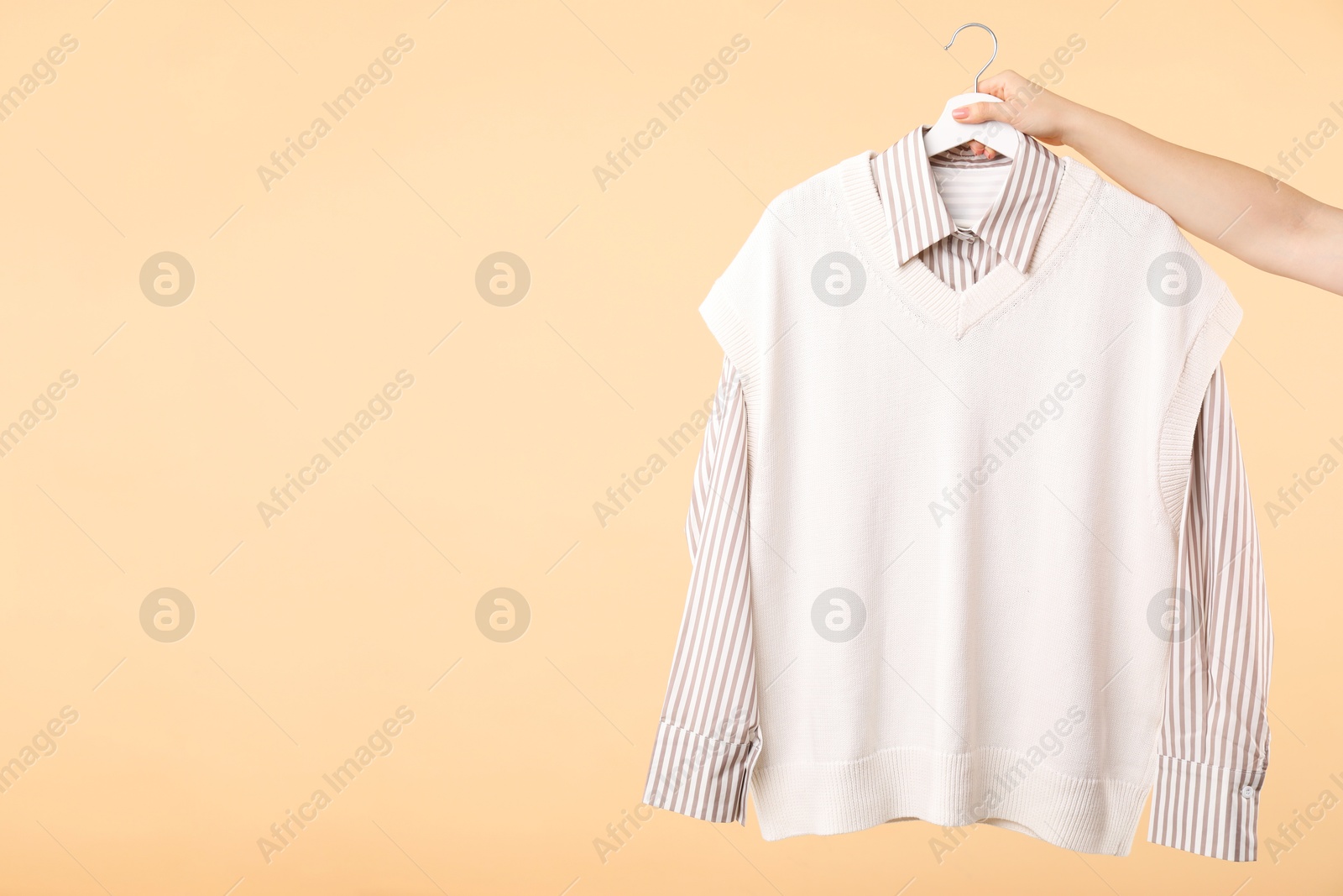 Photo of Woman holding hanger with beautiful clothes on beige background, closeup. Space for text