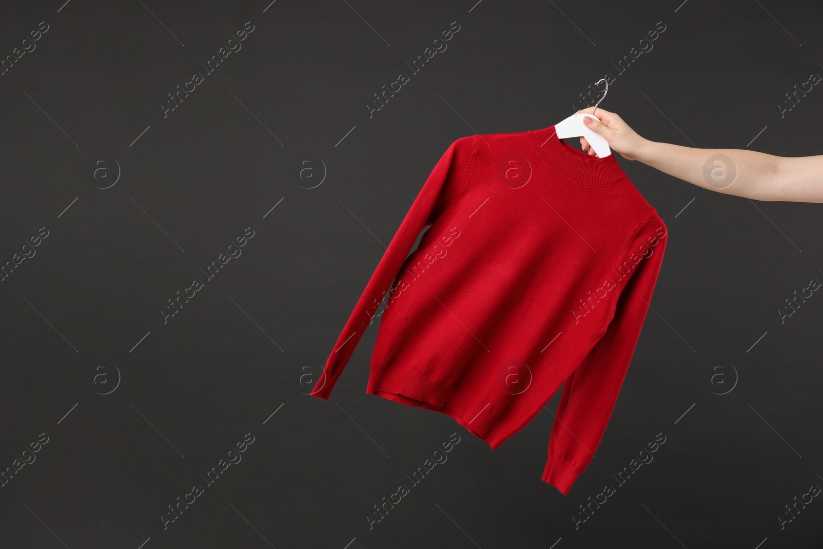 Photo of Woman holding hanger with red sweater on black background, closeup. Space for text