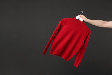 Photo of Woman holding hanger with red sweater on black background, closeup. Space for text