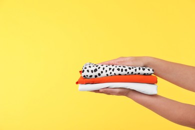 Photo of Woman holding stack of clothes on yellow background, closeup. Space for text