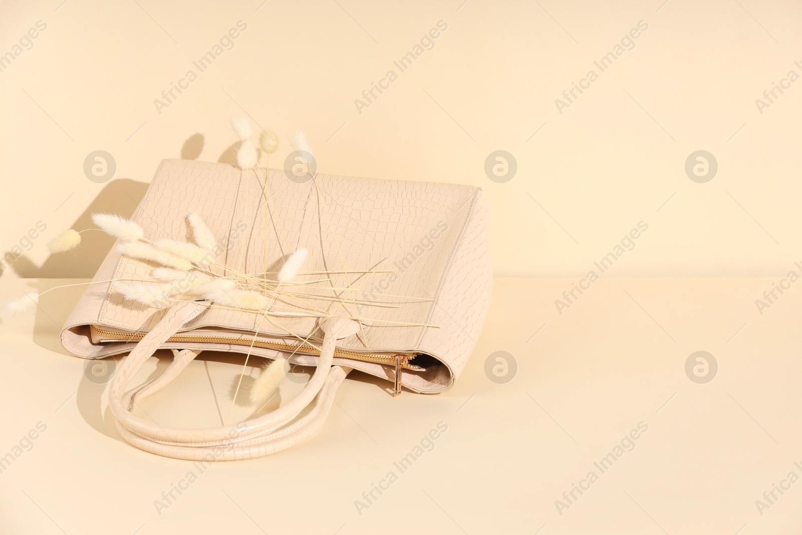 Photo of Bag and dry flowers on beige background, space for text